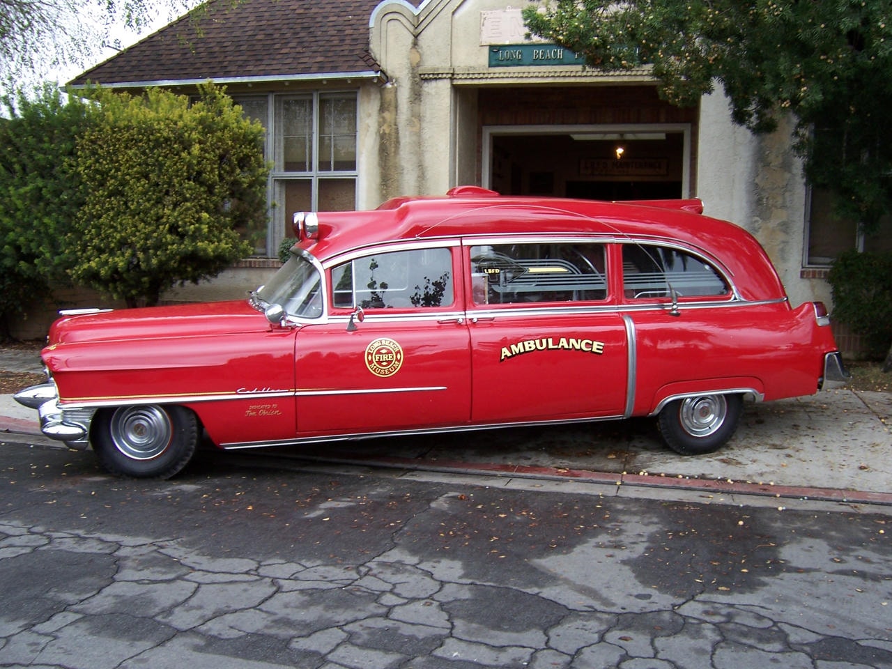 1955 Cadillac ambulance in red with Long Beach Fire Museum emblem parked outside the engine house