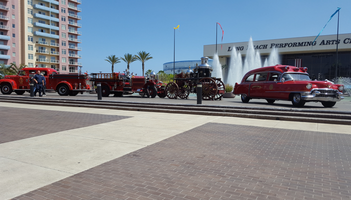 Four historic Long Beach fire vehicles on display at a fire chiefs convention — 1958 Mack B125, 1924 Ahrens-Fox, 1907 Amoskeag steam pumper, and 1955 Cadillac ambulance